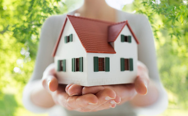 real estate, accommodation and property concept - close up of hands holding house or home model over green natural background