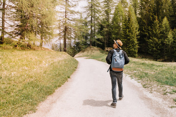 Male traveler with big blue backpack going to forest thicket and looks around with interest. Young man in elegant hat enjoying nature views during trip to pinery in sunny warm day.