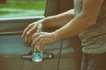 Man opening his car while holding a bottle of alcohol