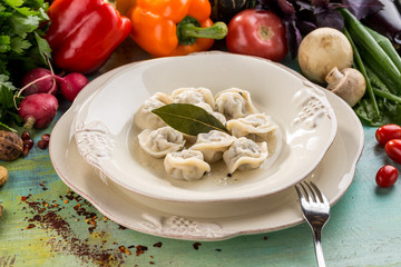 Russian meat dumplings pelmeni with bay leaf and fresh vegetables on blue wooden table