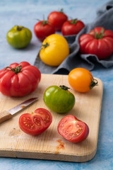verschiedene Tomaten teilweise angeschnitten auf holzbrett und hellem untergrund hochformat