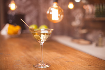 Tasty white martini with green olives on a stick in a restaurant bar counter