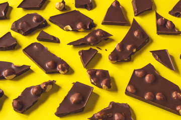 Broken chocolate bar with hazelnuts on yellow background, closeup