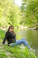 Woman poses sitting next to a river of a public park enjoying nature