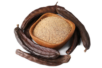 Ground carob (Ceratonia siliqua) powder with carob bean pods isolated on white background