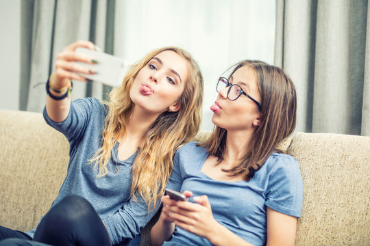 Two teen girls smile and take a selfie together. They make grimaces out of their tongue