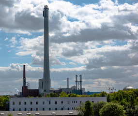 View of a combined heat and power plant with a long chimney in front of a dramatic sky covered with clouds.