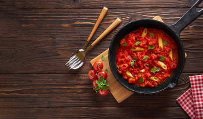 Pasta penne with tomato sauce and basil on iron cast pan. Wooden table, top view with copy space