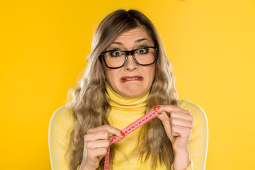 A horified blonde with glasses, holding a measuring tape on yellow background