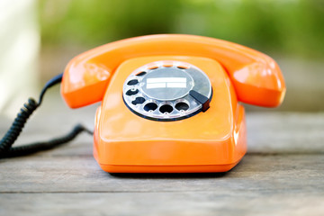 Retro phone orange color, handset receiver on wooden textured background. Shallow depth field photography.
