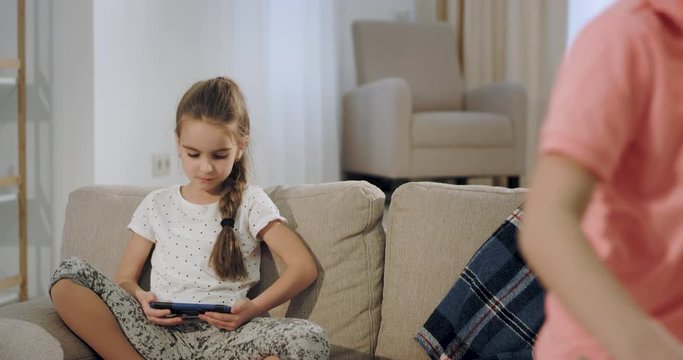 Big brother and small sister have a time together after school they take a sit on the sofa and take a smartphone to play a game. 4k