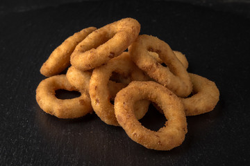 Rings of onions or squid in batter on black background. Snack to beer. Snack to beer. Fast food.