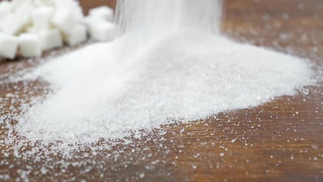White granulated sugar and refined sugar on brown wooden surface