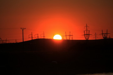 sunset through voltage poles on the hill