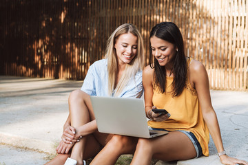 Two smiling young girls using laptop at the park