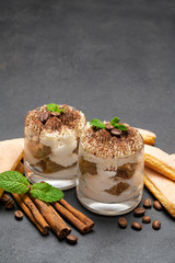 Classic tiramisu dessert in a glass and savoiardi cookies on dark concrete background