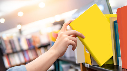 Bestseller publishing concept. Male hand choosing and picking yellow book from wooden bookshelf in bookstore. Education research in university public library. - obrazy, fototapety, plakaty