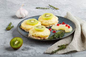Pieces of baked pork with pineapple, cheese and kiwi on gray background.