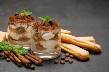 Classic tiramisu dessert in a glass and savoiardi cookies on dark concrete background