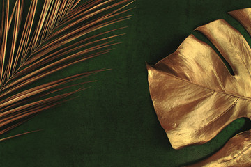 Closeup of golden palm and monstera leaves on abstract dark green textured background. Tropical conceptual elegant trendy summer background. Flat lay. Copy space.