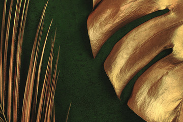 Closeup of golden palm and monstera leaves on abstract dark green textured background. Tropical conceptual elegant trendy summer background. Flat lay. Copy space.
