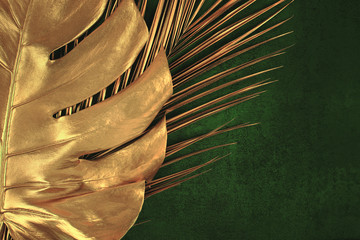 Closeup of golden palm and monstera leaves on abstract dark green textured background. Tropical...