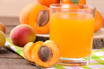 Apricot juice in a glass cup next to fresh apricots on a brown wooden background