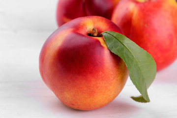 Ripe large nectarines with a green leaf close-up on a white wooden background