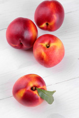 Ripe large nectarines with a green leaf close-up on a white wooden background