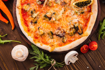 delicious Italian seafood pizza with ingredients on a dark wooden table (close top view).