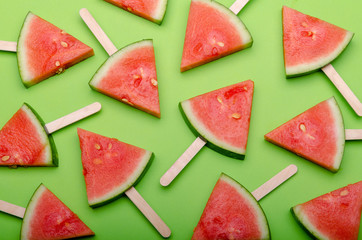 slices of watermelons as popsicle on green background