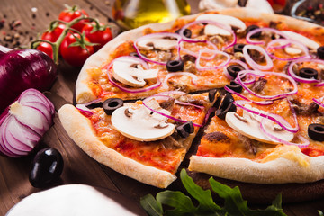 Italian pizza with mushrooms, olives and onion rings with ingredients on wooden table (close). Cut one piece