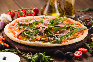 Pizza with bacon and arugula on a dark wooden background with ingredients around (close).