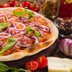 Italian pizza with chicken, onions and rucola leaves on a dark wooden background with ingredients...
