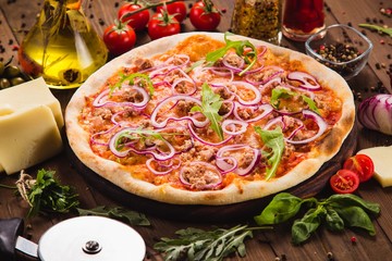 Italian pizza with chicken, onions and rucola leaves on a dark wooden background with ingredients around (close)