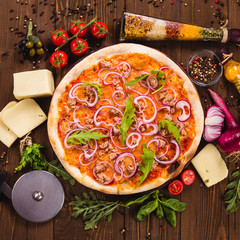 Italian pizza with chicken, onions and rucola leaves on a dark wooden background with ingredients...