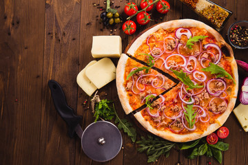 Italian pizza with chicken, onions and rucola leaves on a dark wooden background with ingredients...