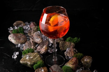 Fototapeta na wymiar Aperol syringe soft alcoholic drink on a black background with stones and ice. Cocktail card for a bar or restaurant.