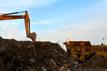 Heavy excavator bucket working in quarry on a background of sunset and blue sky. Mobile jaw stone...