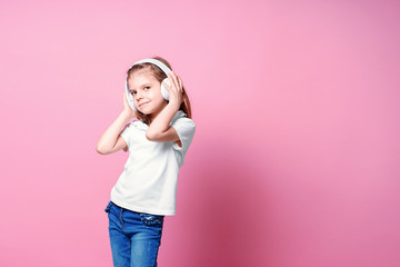 Girl listening to music in headphones on pink background. Cute child enjoying happy dance music, smile, posing on pink studio background wall.