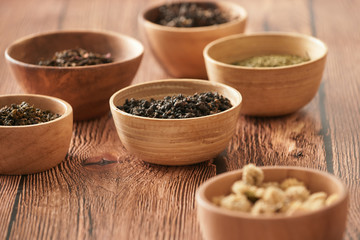 assortment of dry tea in white bowls on wooden surface
