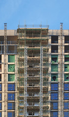 modern multistory apartment building under construction with scaffolding and hoist frames under a blue sky