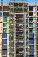 tall modern multistory apartment building under construction with scaffolding and hoist frames under a blue sky