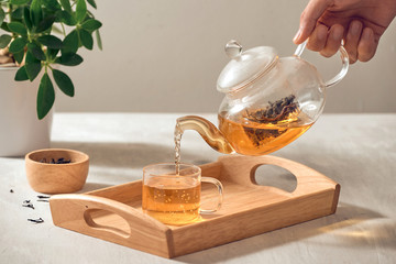 A hand pouring tea from glass teapot on wooden serving tray - 266895221