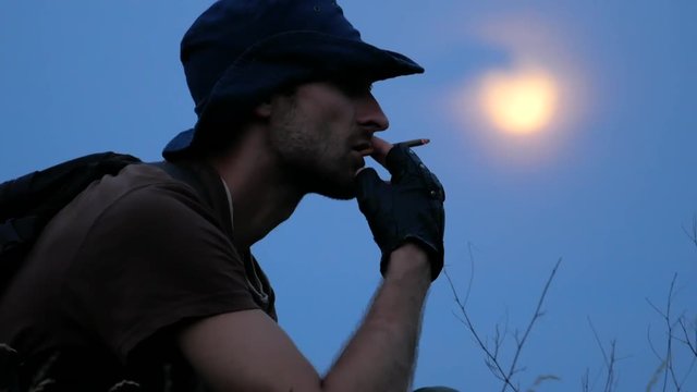 Close-up of smoking traveler who resting at camping with moon