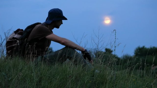 Traveler siting at the grass and resting with full moon at sky