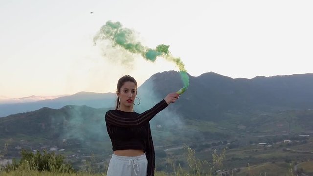 Bellissima ragazza felice, danza in una campagna con prato verde, con dei fumogeni colorati. Video al rallentatore.
