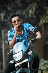A boy looking at camera wearing golden sunglasses and sitting on a motorbike