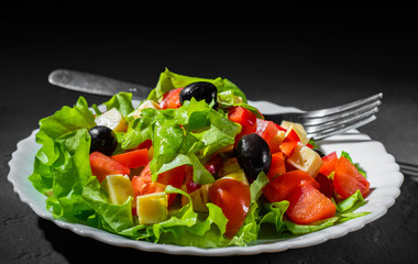 fresh vegetables salad with lettuce, olive, pepper, tomato and cheese in white plate on dark black background