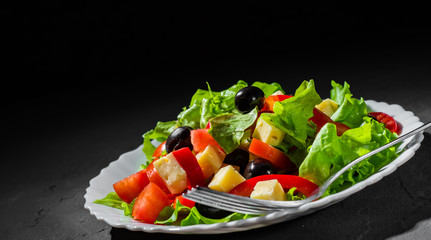 fresh vegetables salad with lettuce, olive, pepper, tomato and cheese in white plate on dark black background